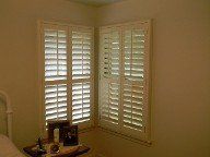 A bedroom with white shutters on the windows and a bed.