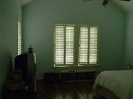 A bedroom with a bed , television , and shutters on the windows.