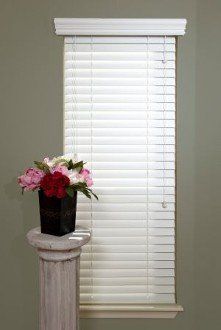 A vase of flowers is sitting on a pedestal in front of a window with blinds.