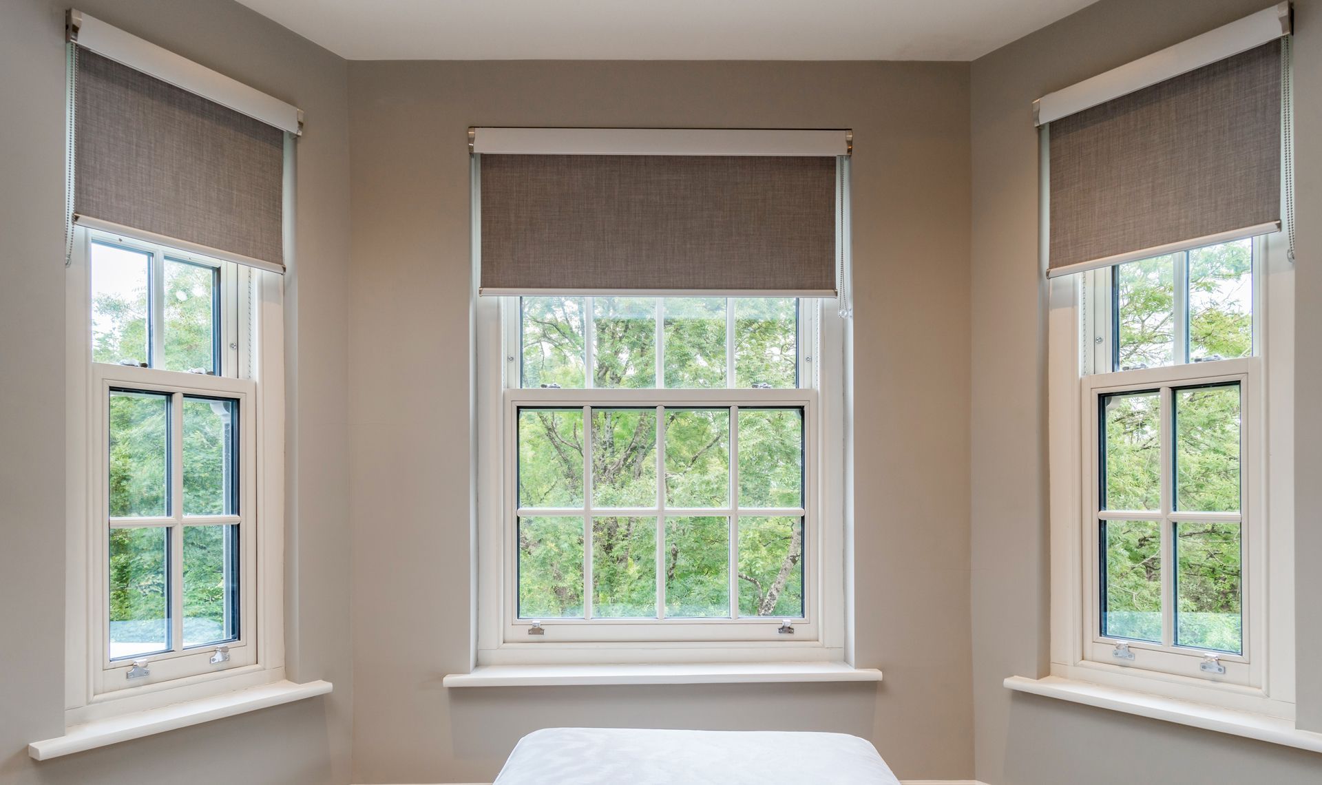 A bedroom with three windows and a bed in the corner.