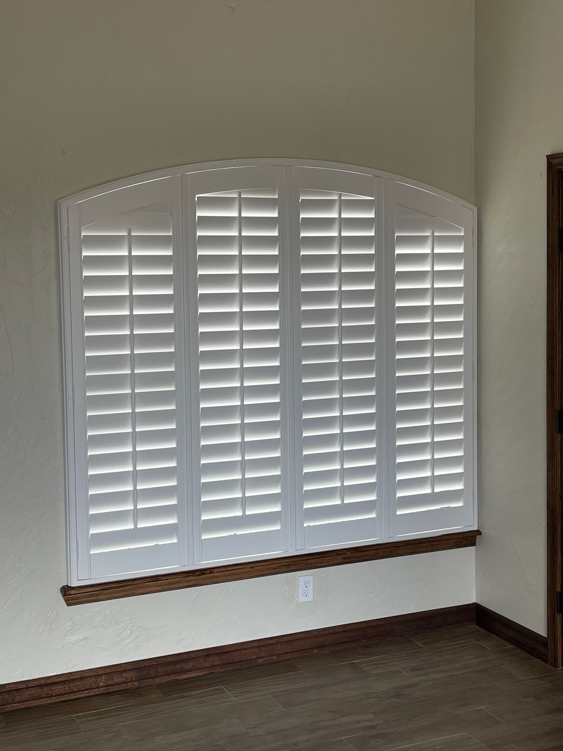 A room with a window with white shutters on it.
