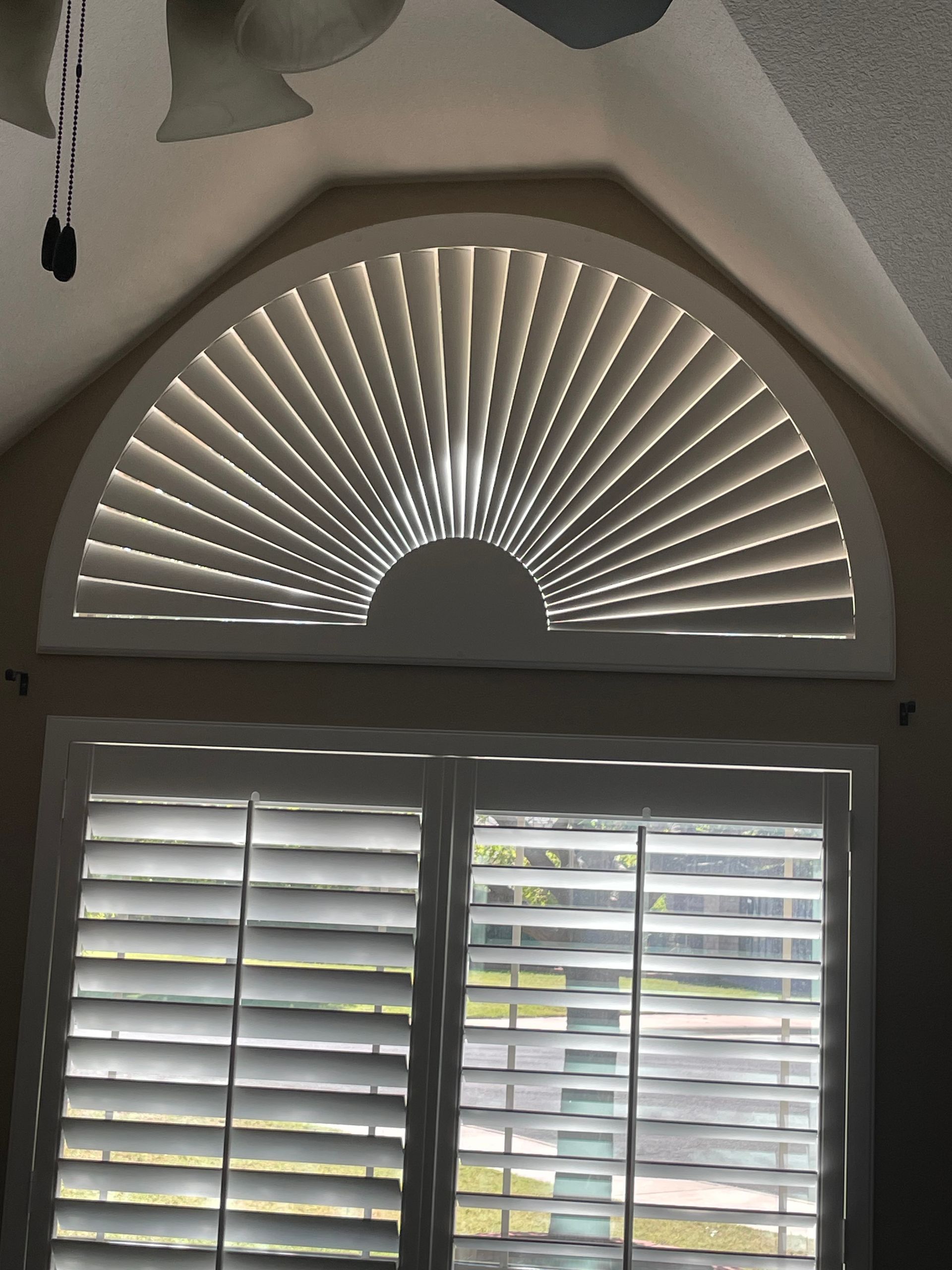 A window with arched shutters and a ceiling fan