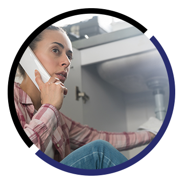 A woman is sitting under a sink talking on a cell phone.