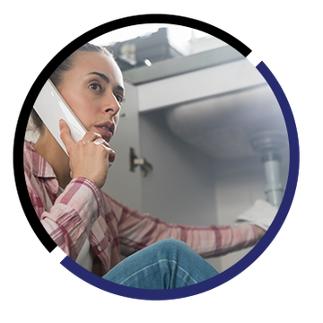 A woman is sitting under a sink talking on a cell phone.