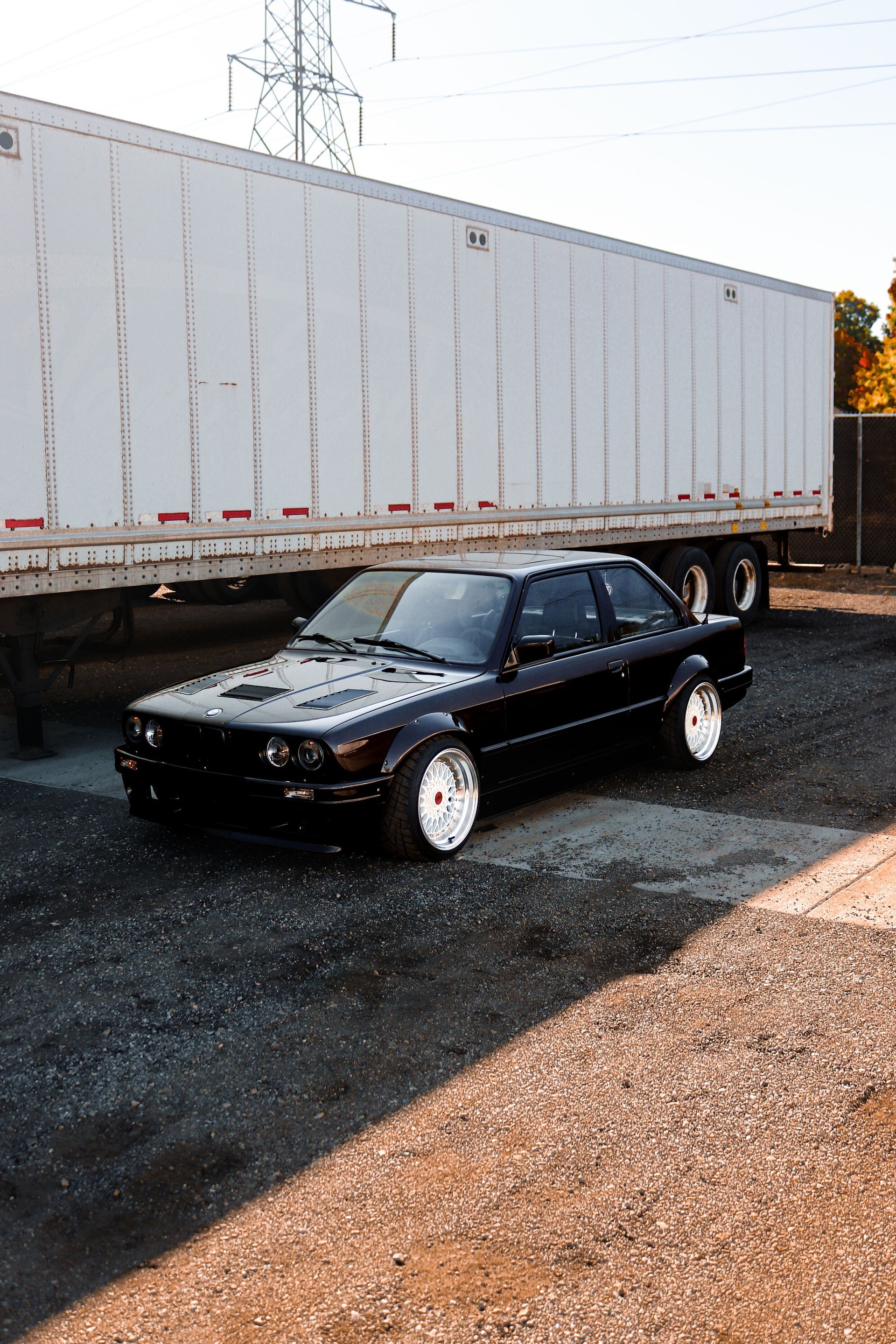 A black car is parked in front of a large white trailer.