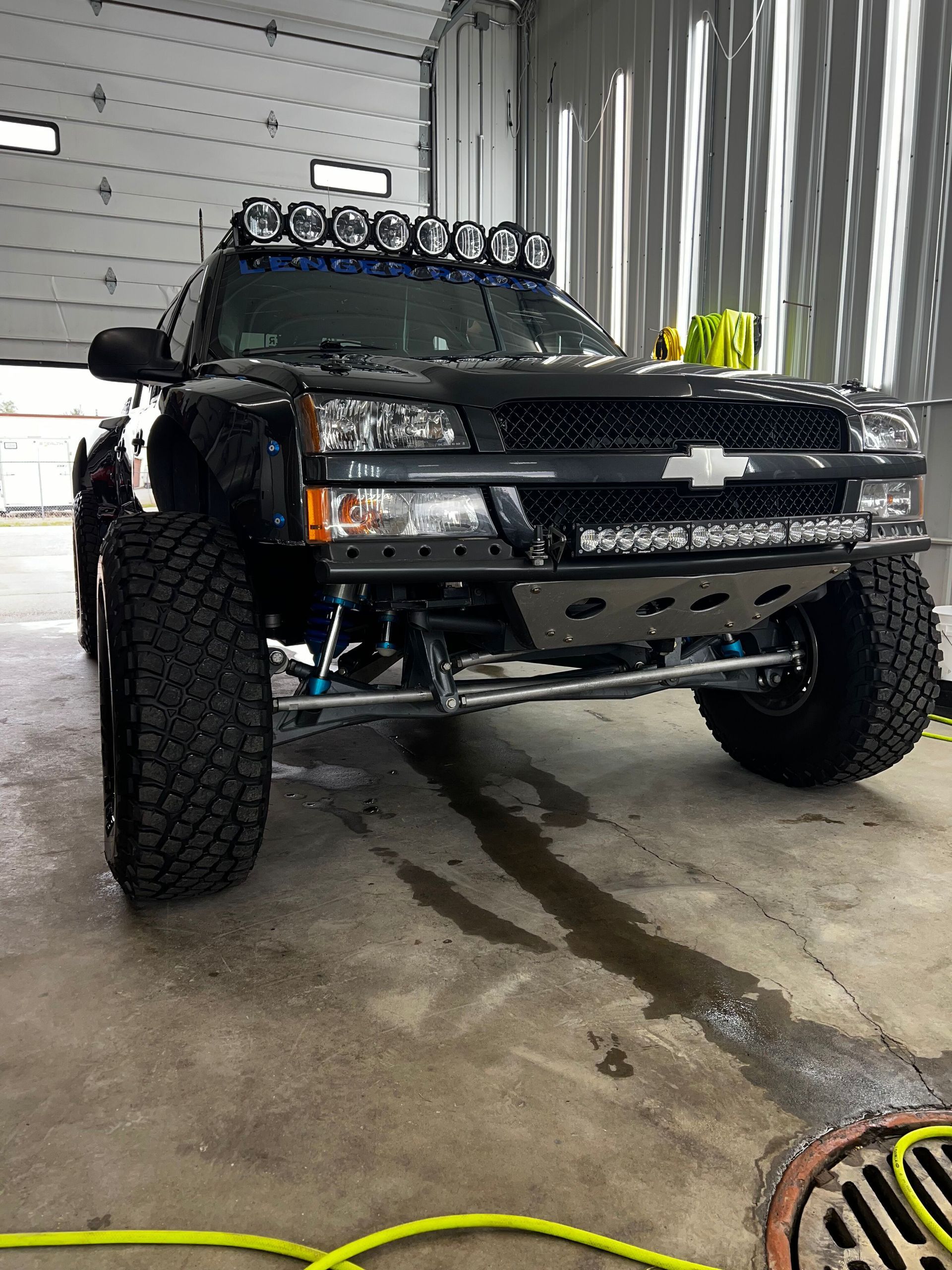 A black truck with a light bar on top of it is parked in a garage.