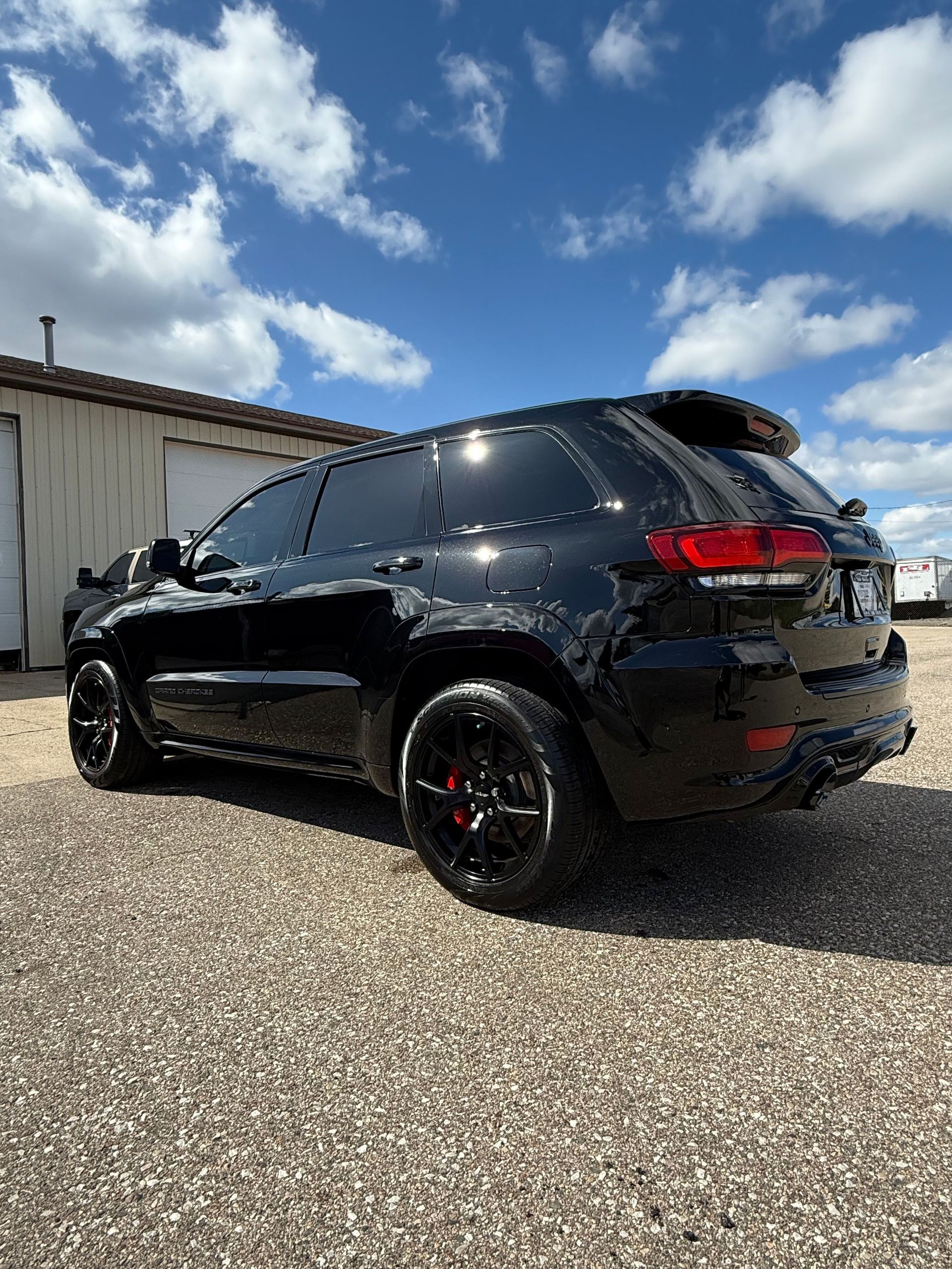 A black jeep grand cherokee is parked in a gravel lot in front of a building.