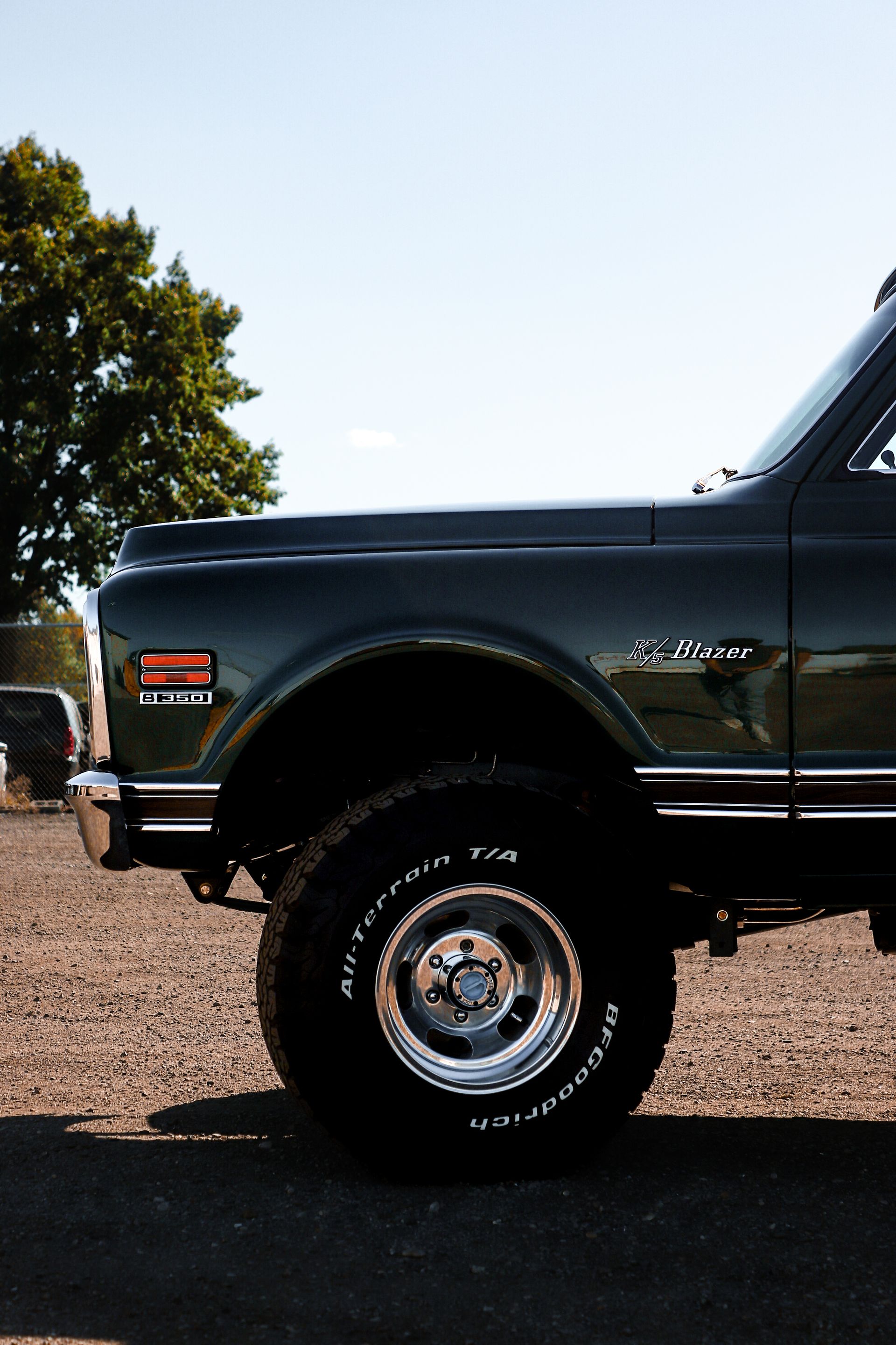 A green truck is parked in a gravel lot.