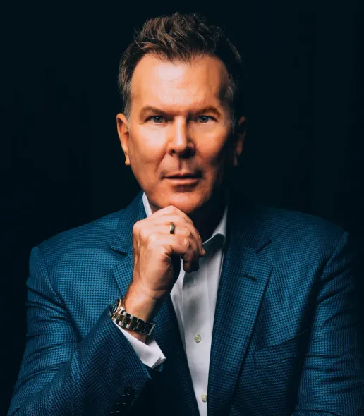 A man in a blue suit and white shirt is holding his hand to his chin.