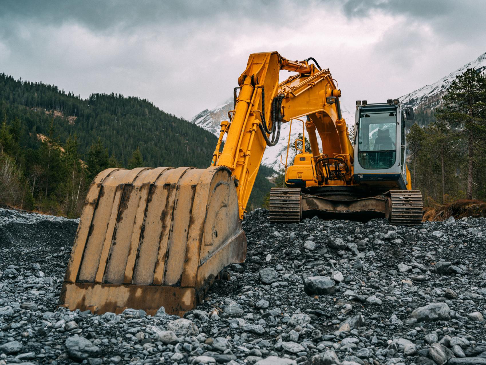 a yellow excavator is sitting on top of a rocky hillside .