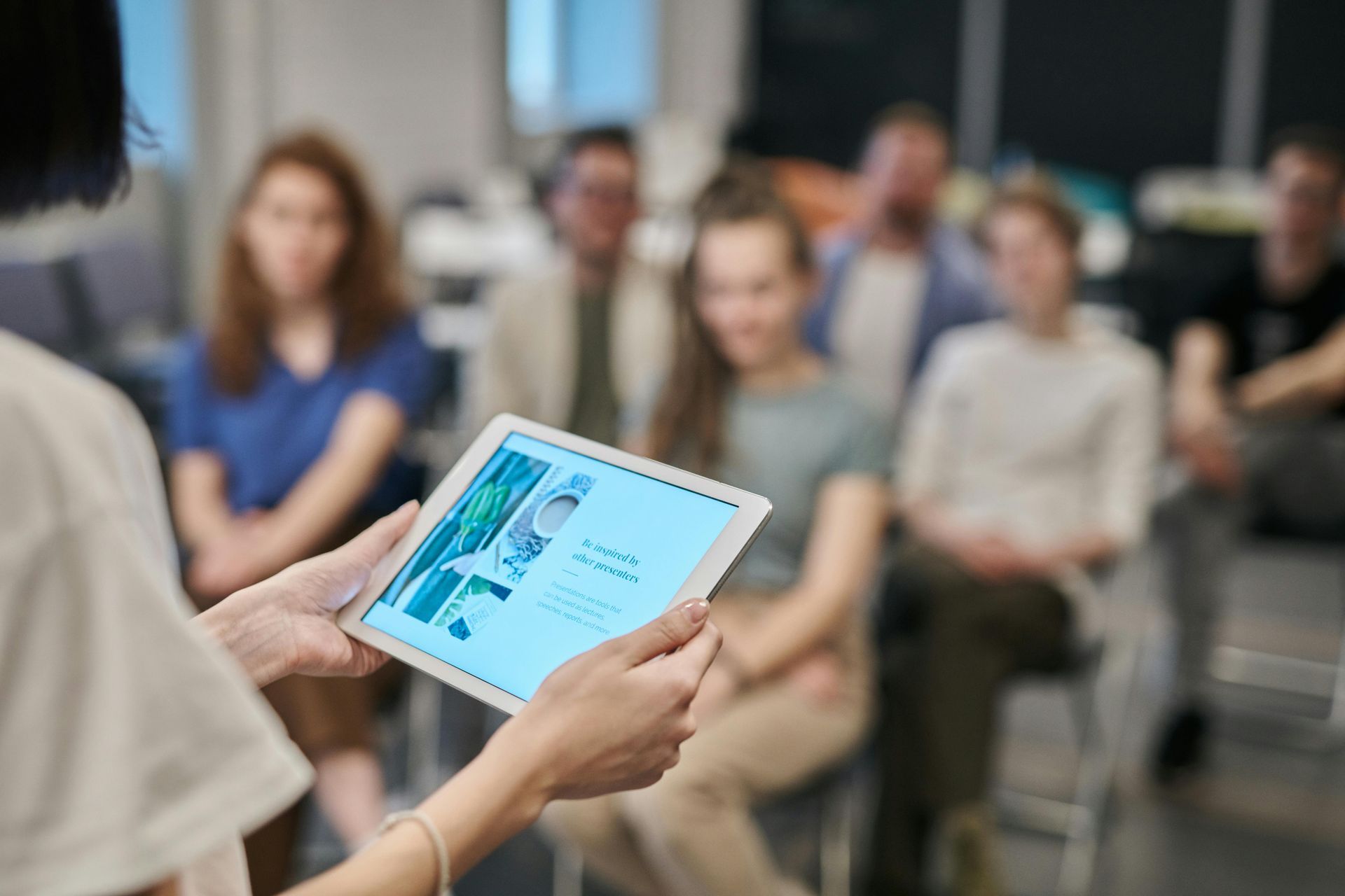 Person presenting information on a tablet to a seated audience.