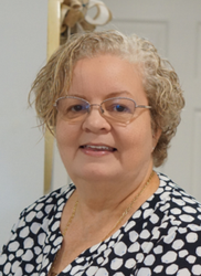 A woman wearing glasses and a polka dot shirt smiles for the camera