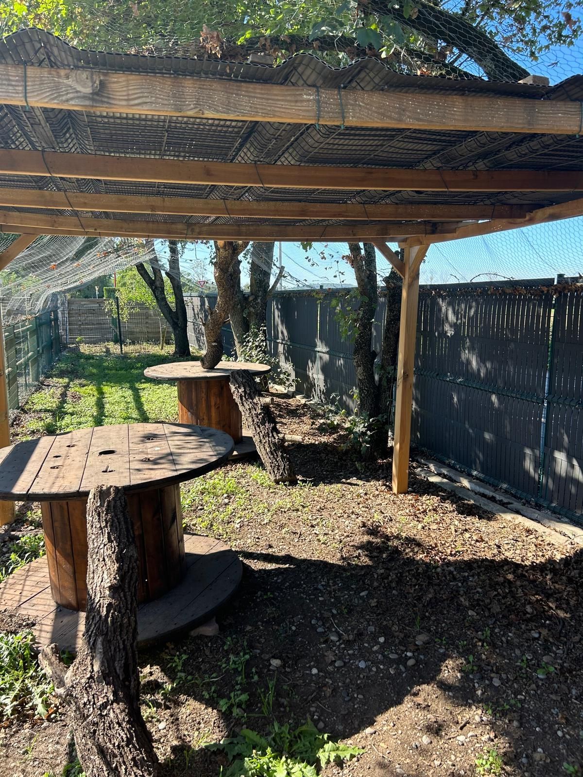 Espace salon extérieur avec tables en bois sous une pergola ombragée.