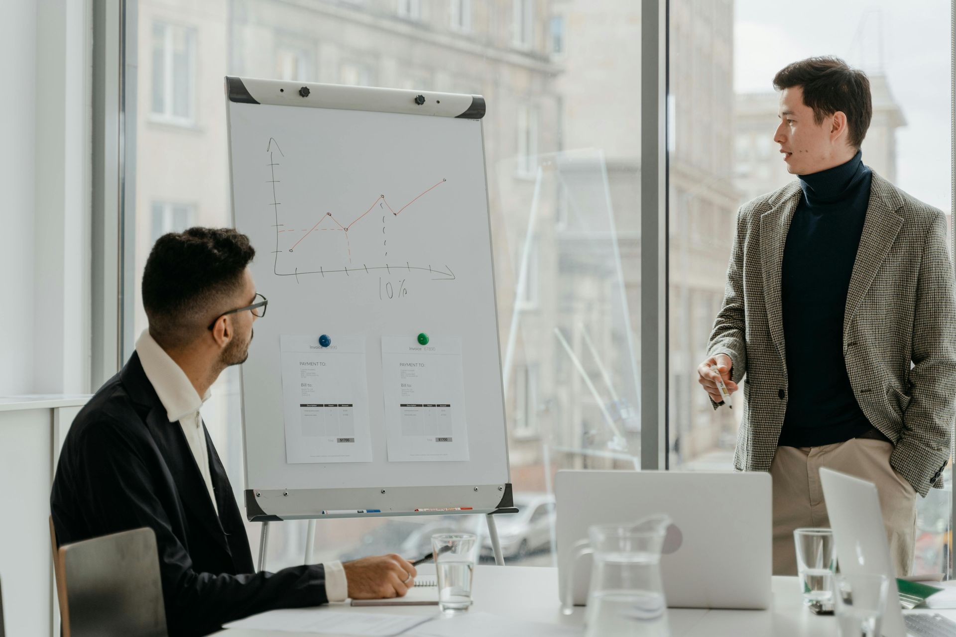 Deux hommes se tiennent devant un tableau blanc dans un bureau.