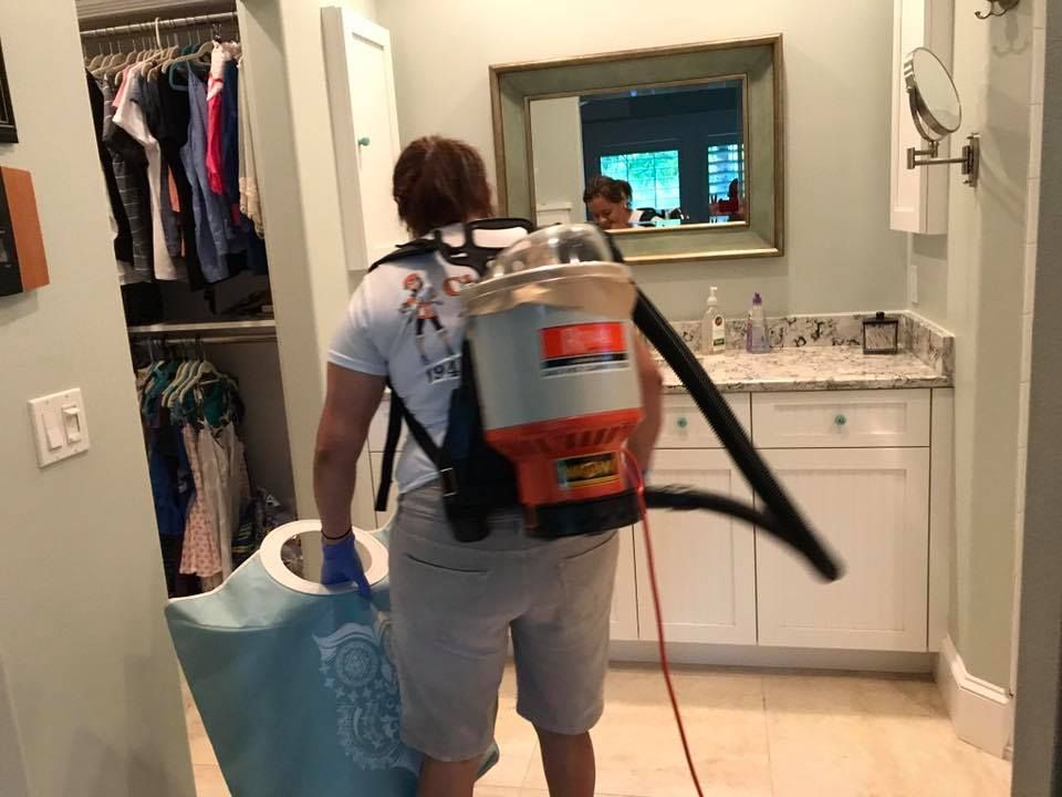 A woman is cleaning a bathroom with a backpack vacuum cleaner.