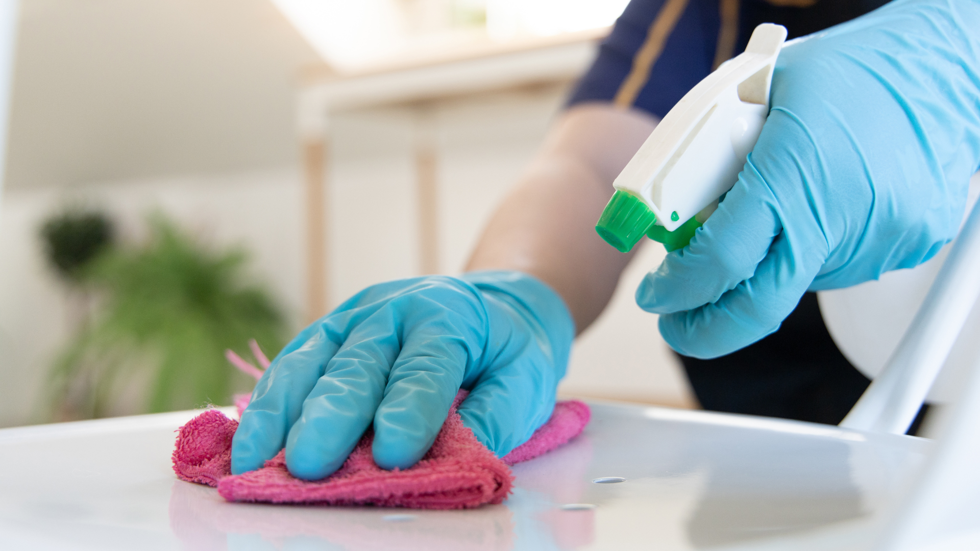 A person wearing blue gloves is cleaning a chair with a cloth and spray bottle.