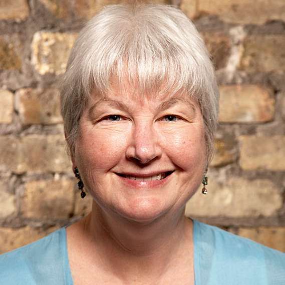 A woman with white hair is smiling in front of a brick wall.