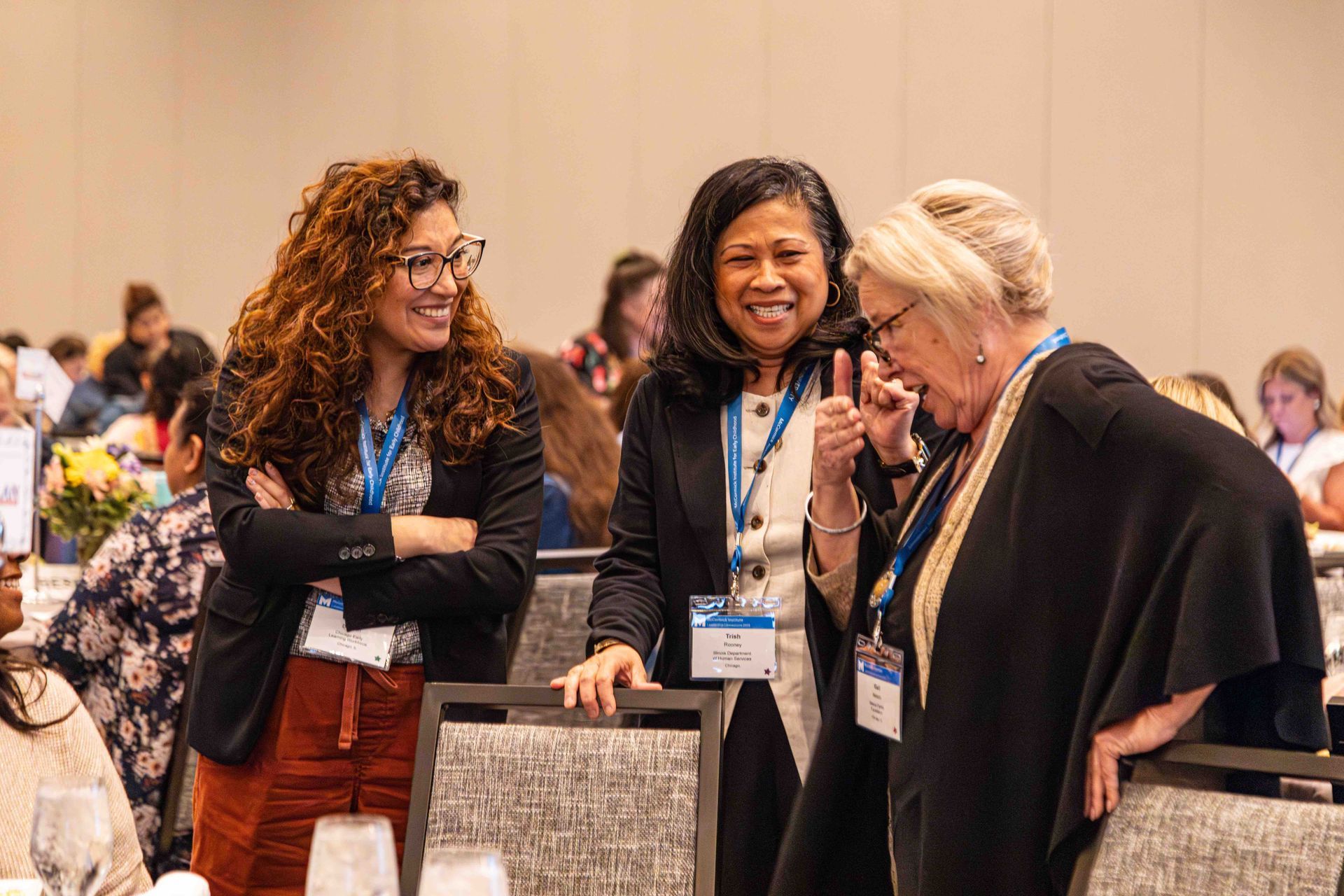 A group of women are standing in a room talking to each other.