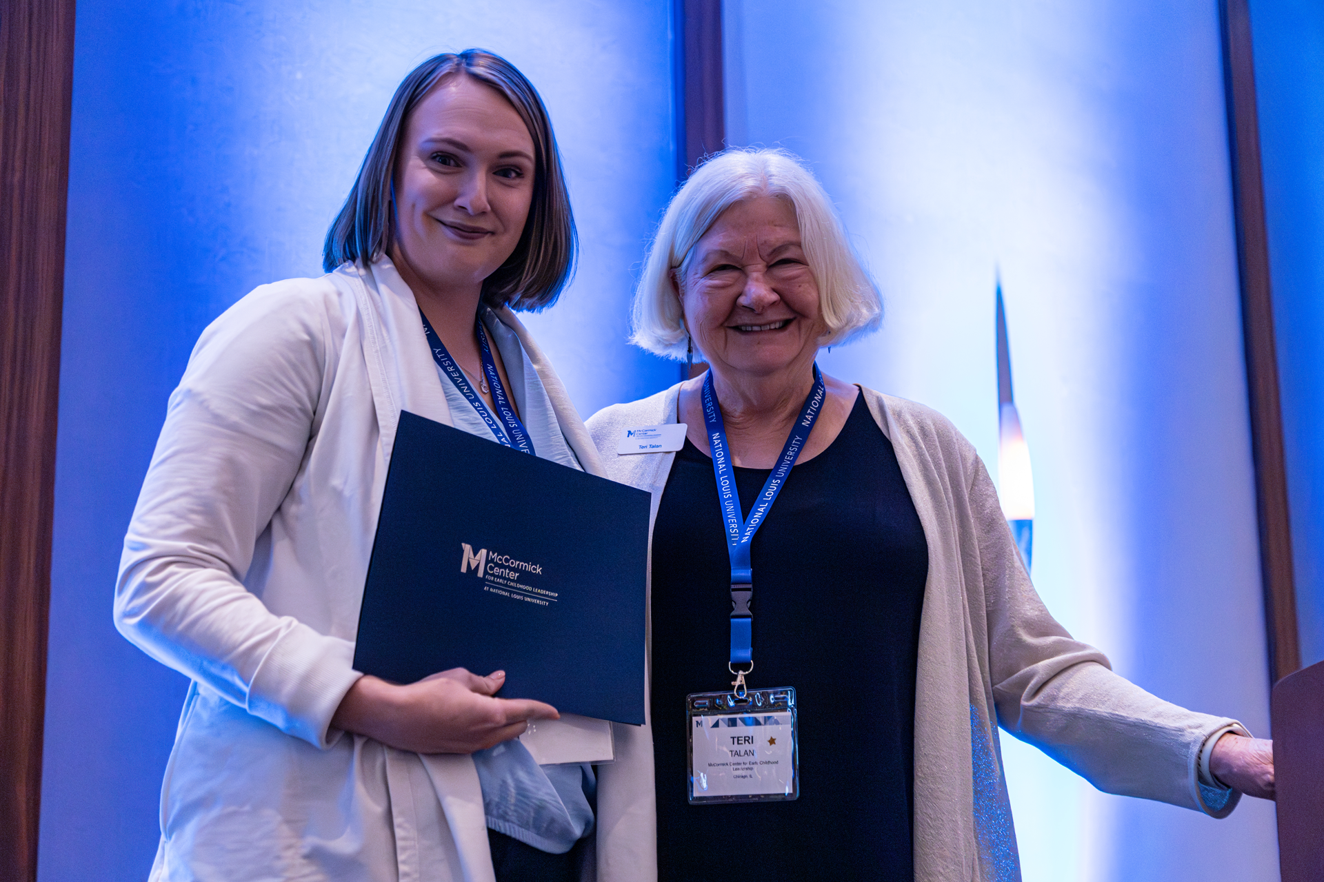 Two women at an event, one holding a certificate. They are both smiling.