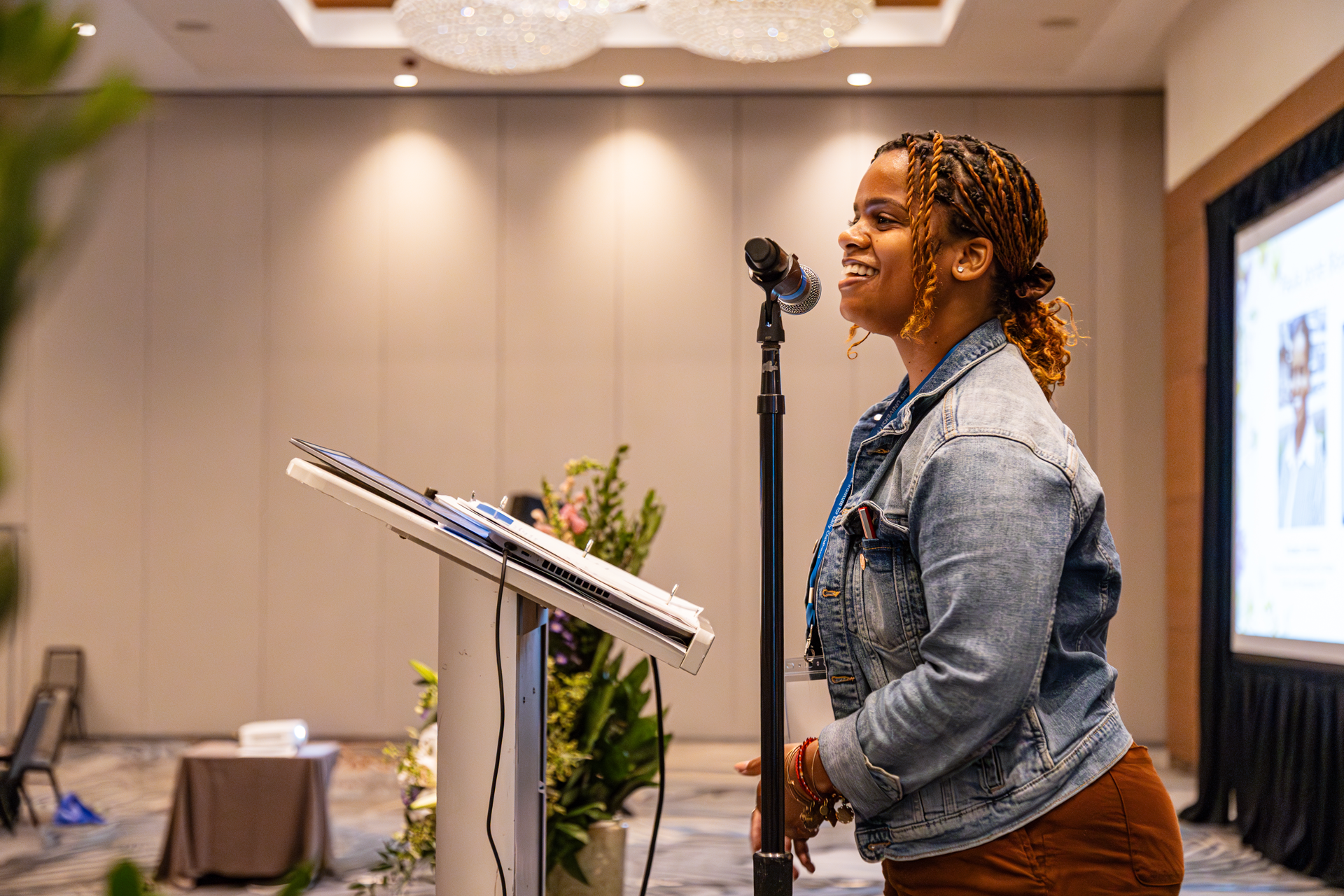 Woman speaking into a microphone at a podium in a conference room.