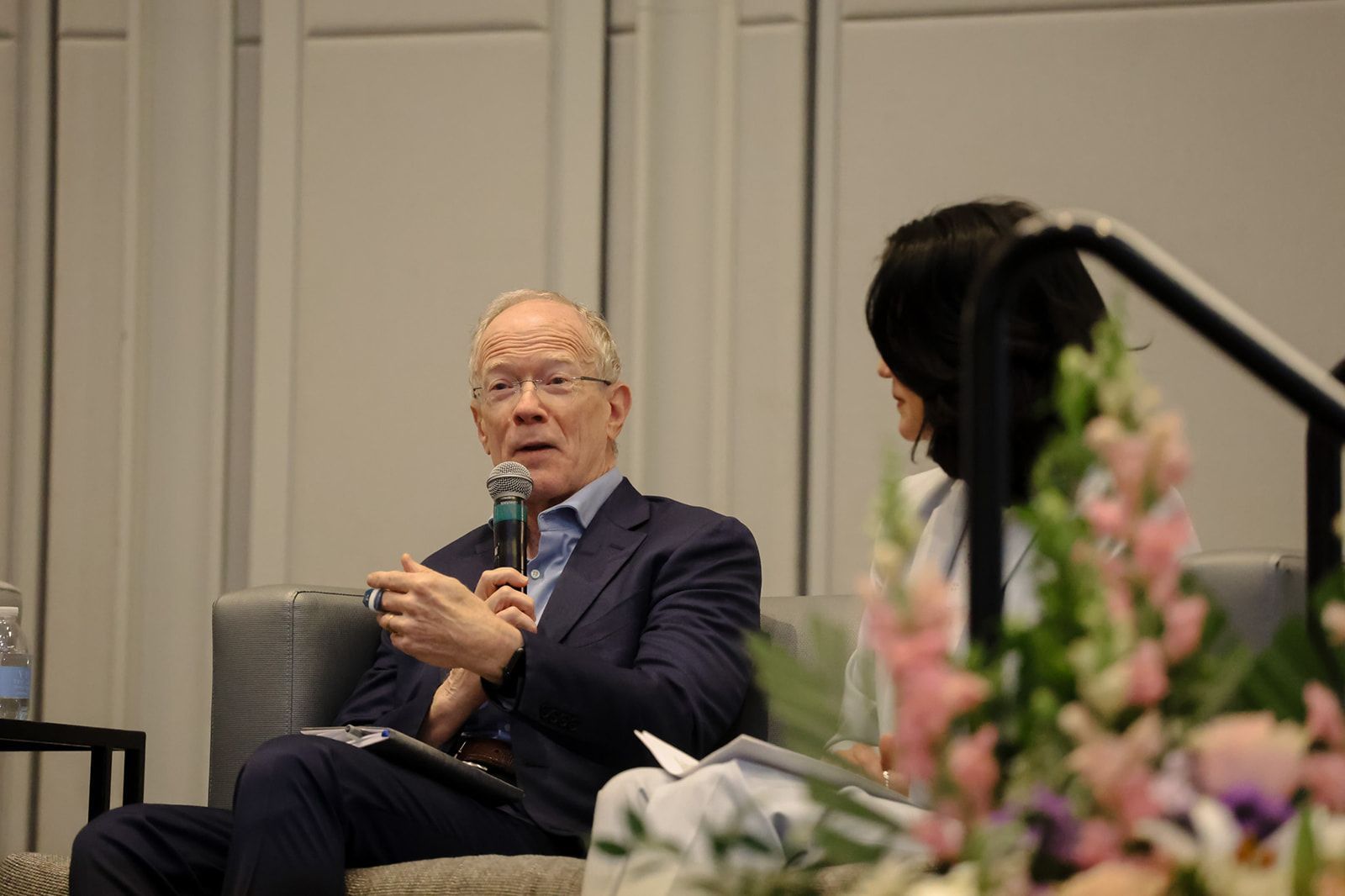 A man in a suit is sitting in a chair talking into a microphone.