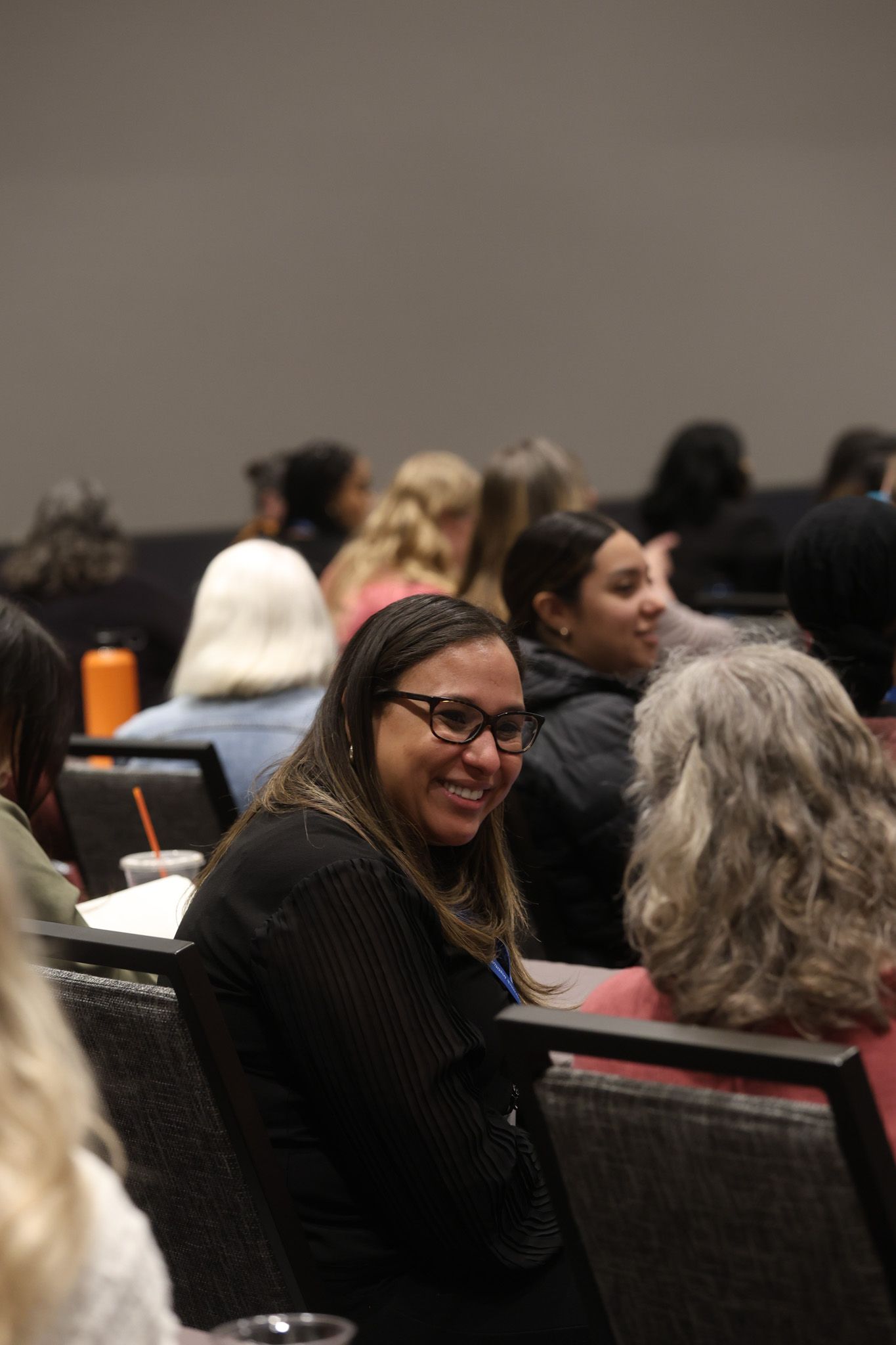 A woman is smiling while sitting in a crowd of people at a conference.