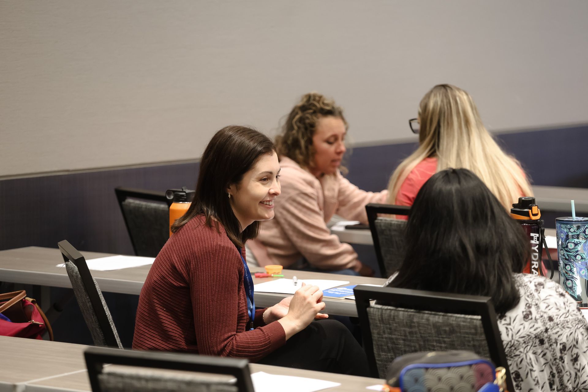 A group of women are sitting at tables in a classroom talking to each other.