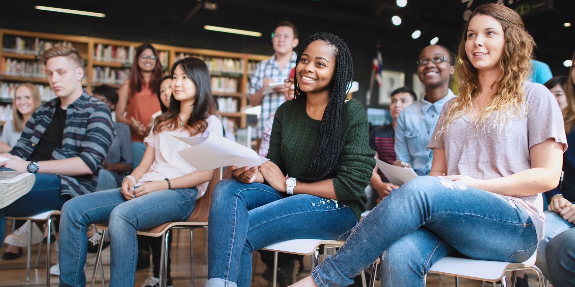 A group of young people are sitting in chairs in a library.