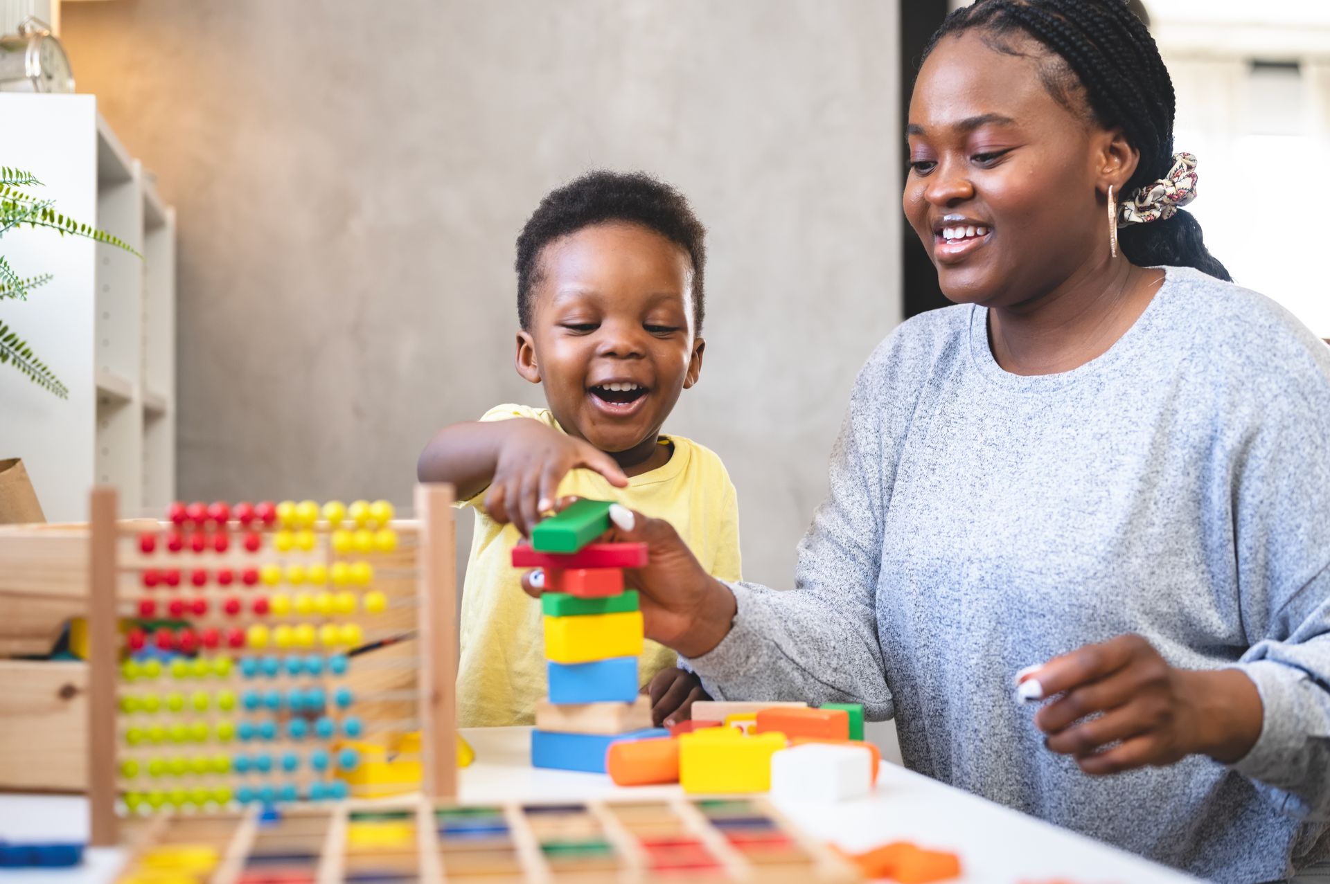 Woman and child stacking colorful blocks, smiling at each other at a table with toys.