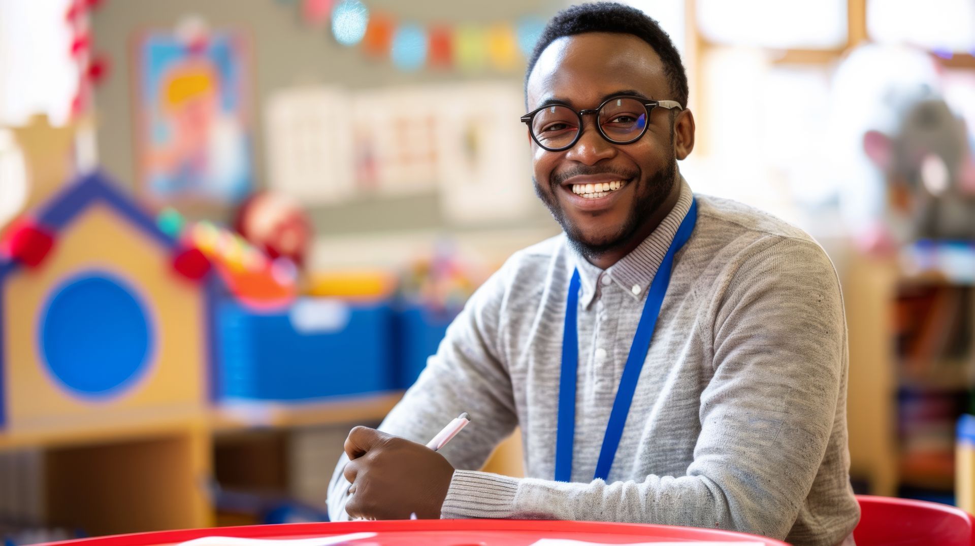 A man wearing glasses is sitting at a table in a classroom.
