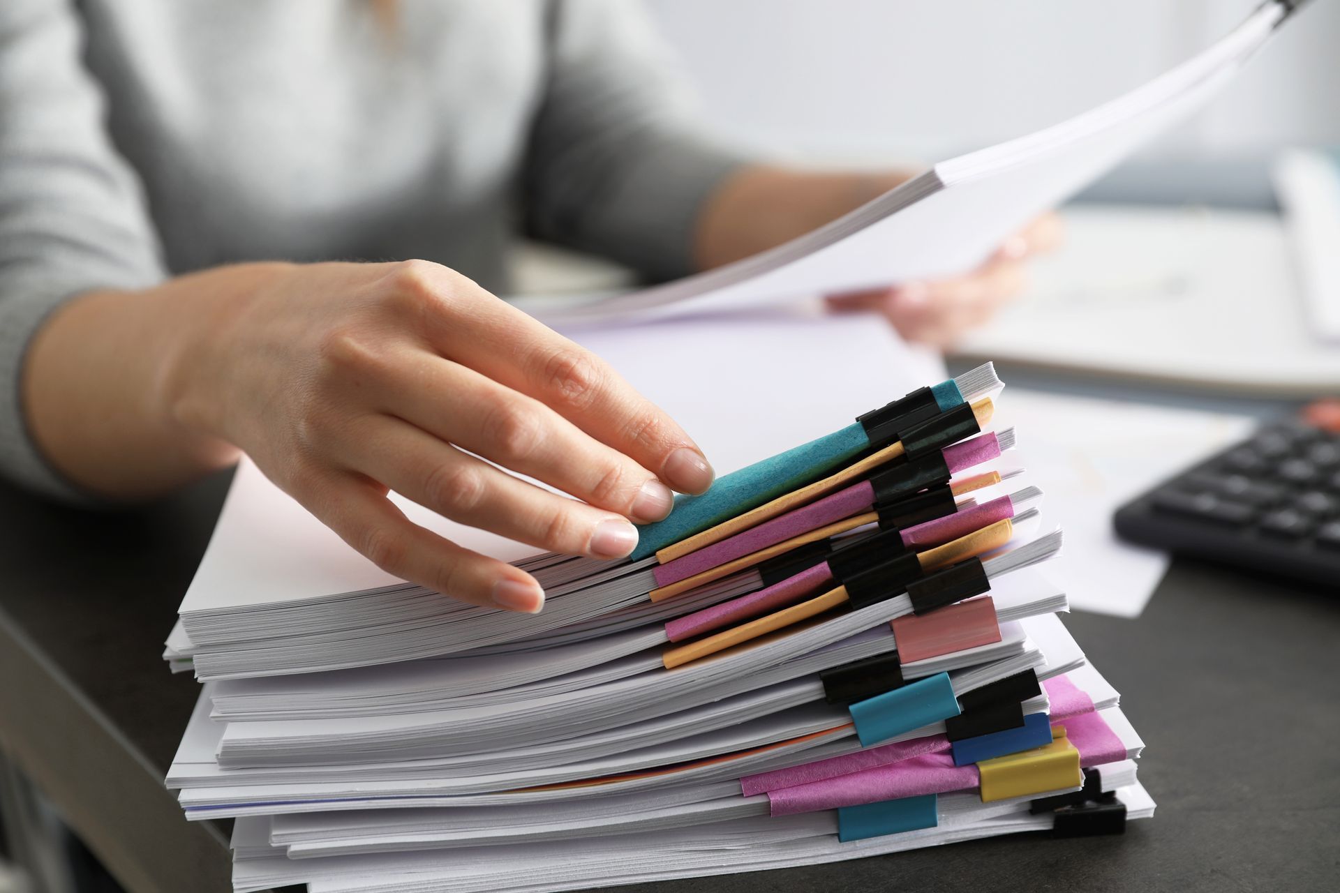Woman sorting through papers clipped with colorful tabs on a desk.