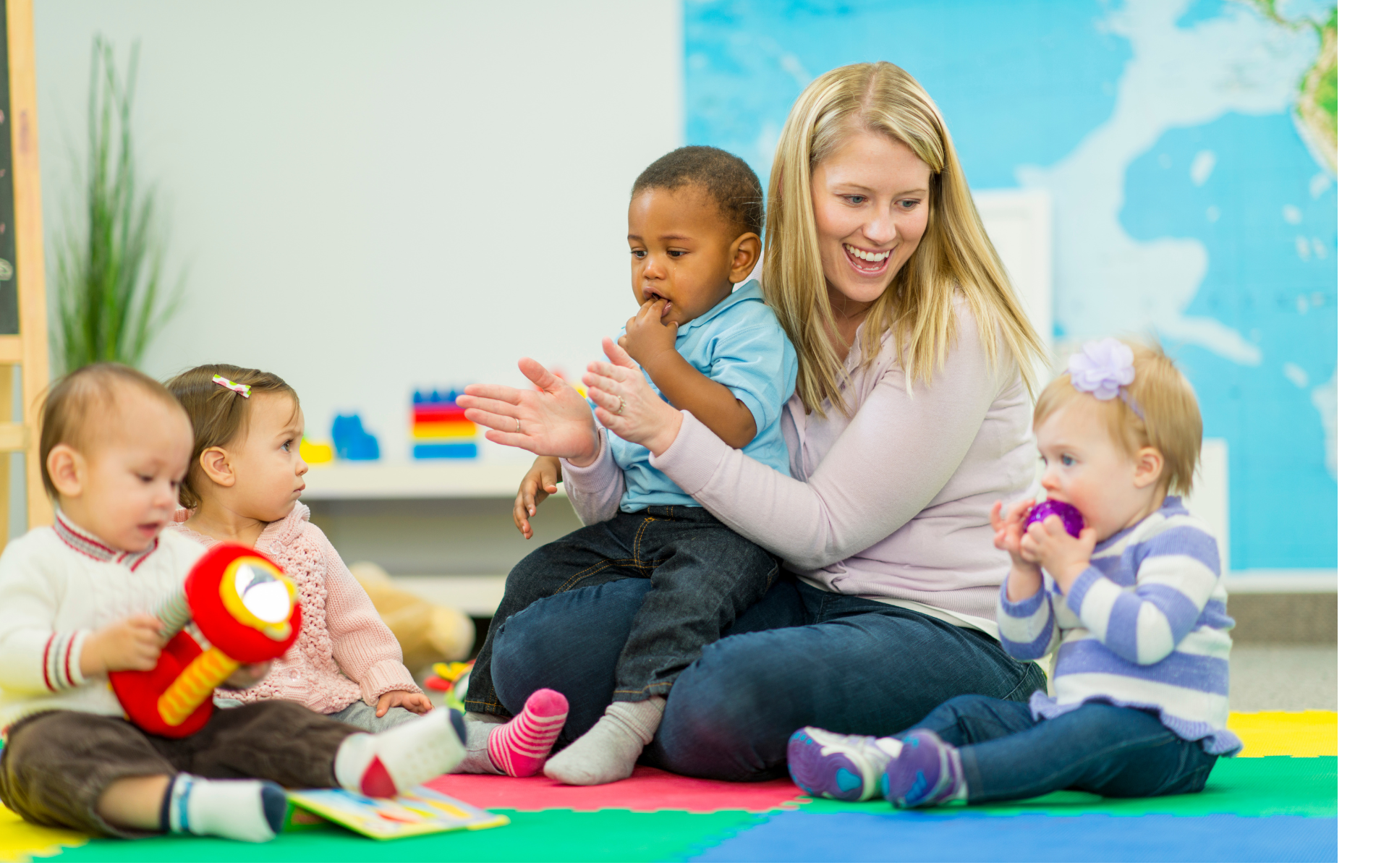 Teacher sits with young children on a colorful mat, clapping.