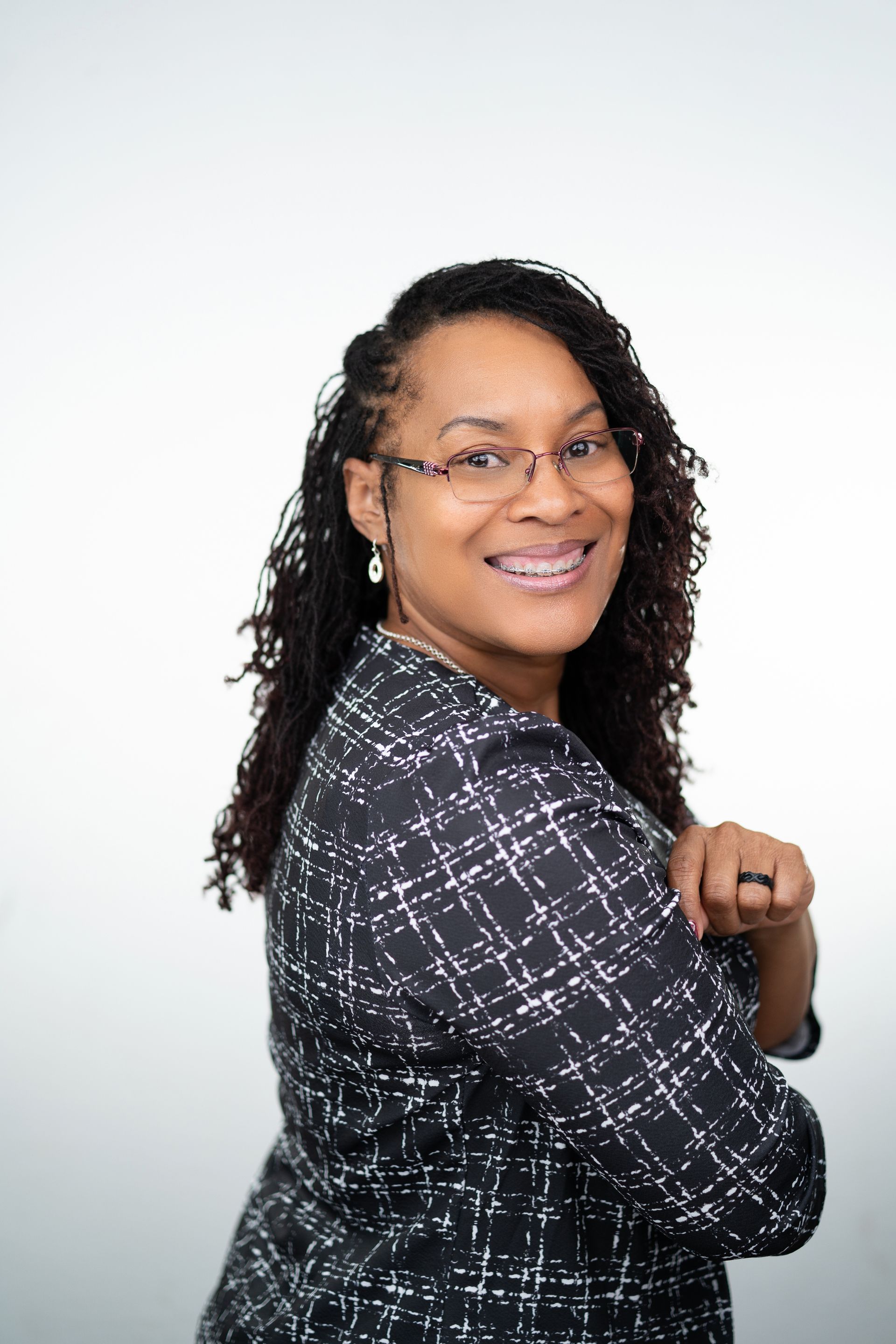 A person wearing glasses and a black patterned blazer smiles while standing against a white background.
