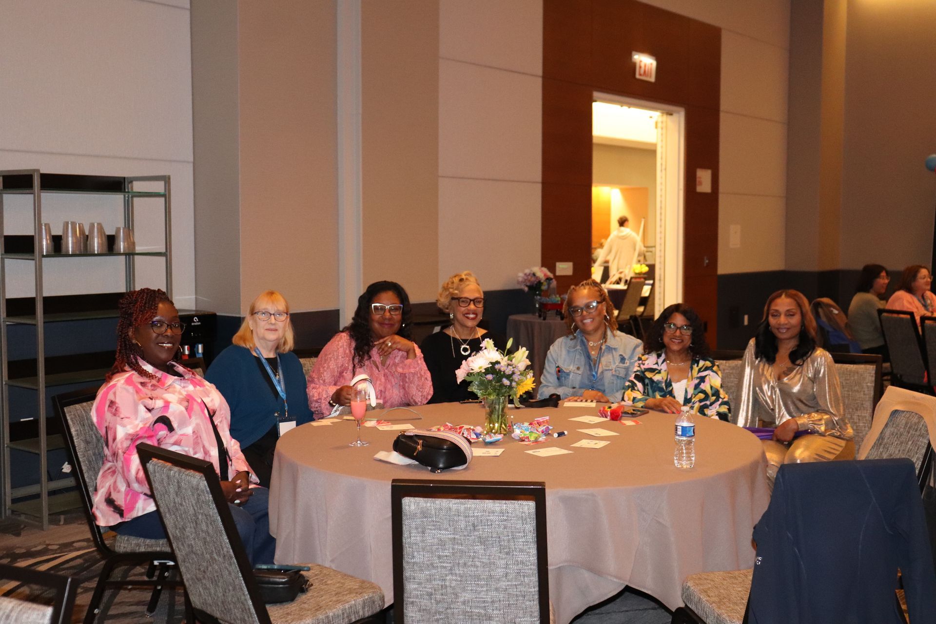 A group of women sit around a round table in a conference setting.