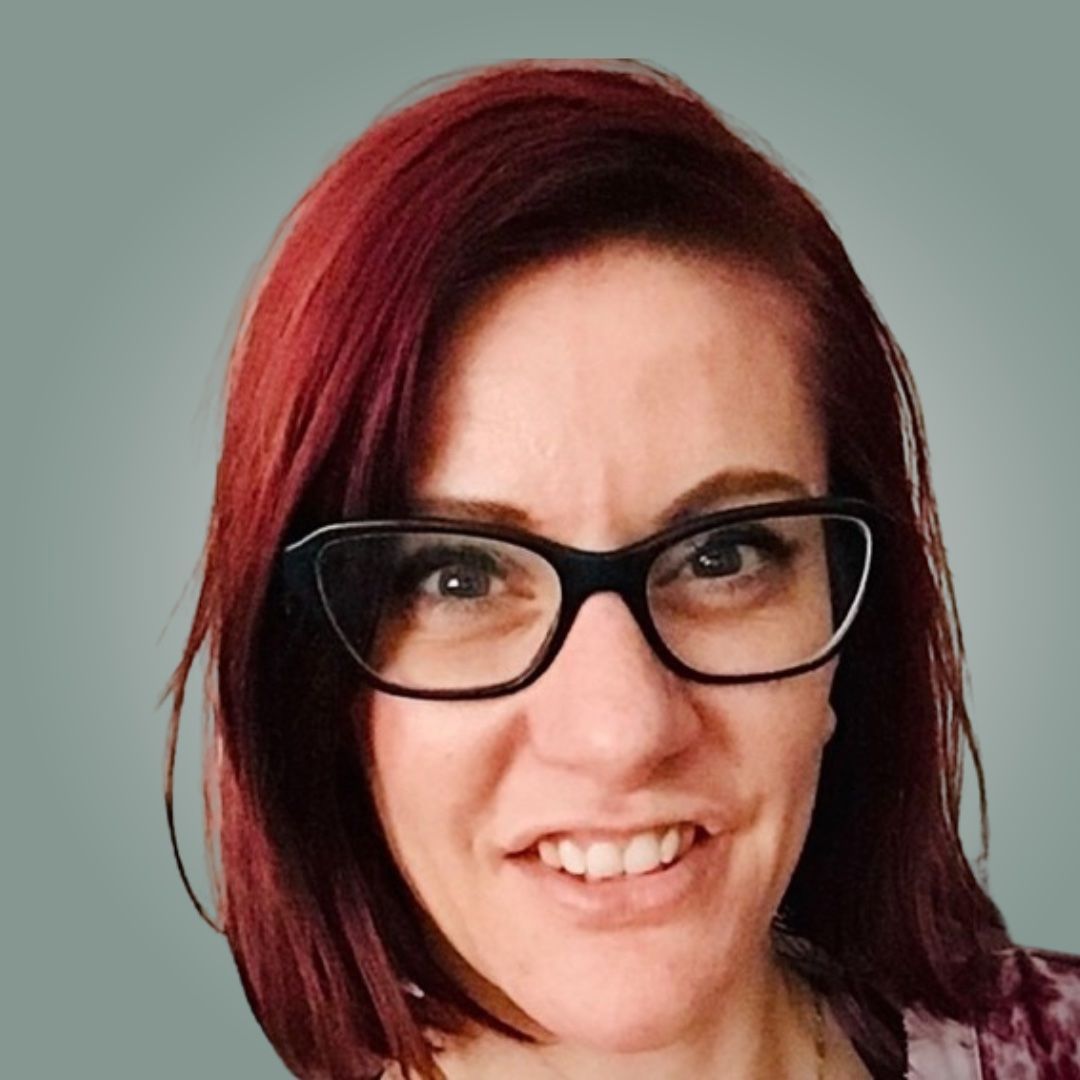 A woman with red hair is wearing glasses and smiling