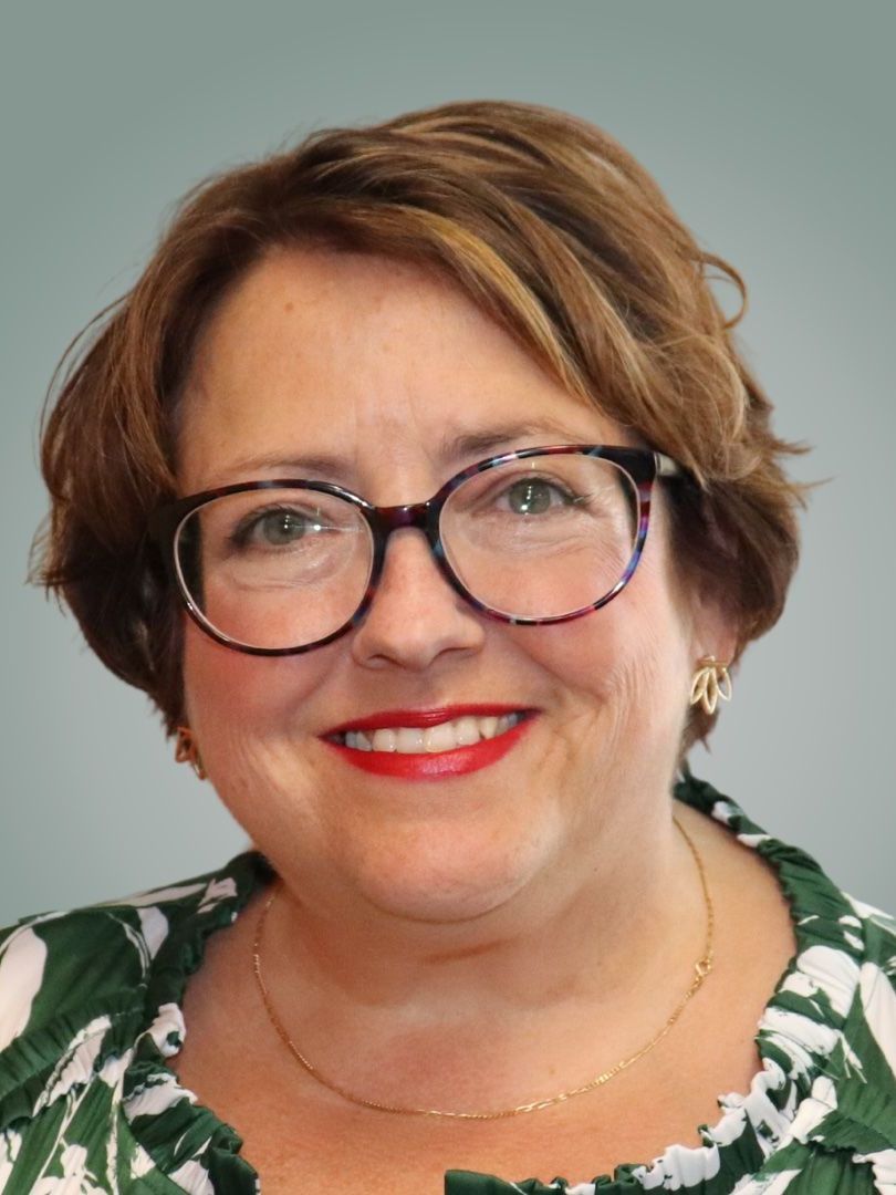 A woman wearing glasses and a green shirt is smiling for the camera.