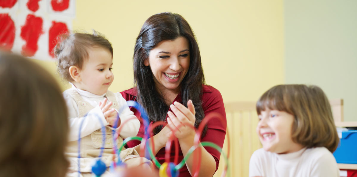 A woman is playing with a baby and two girls in a classroom.