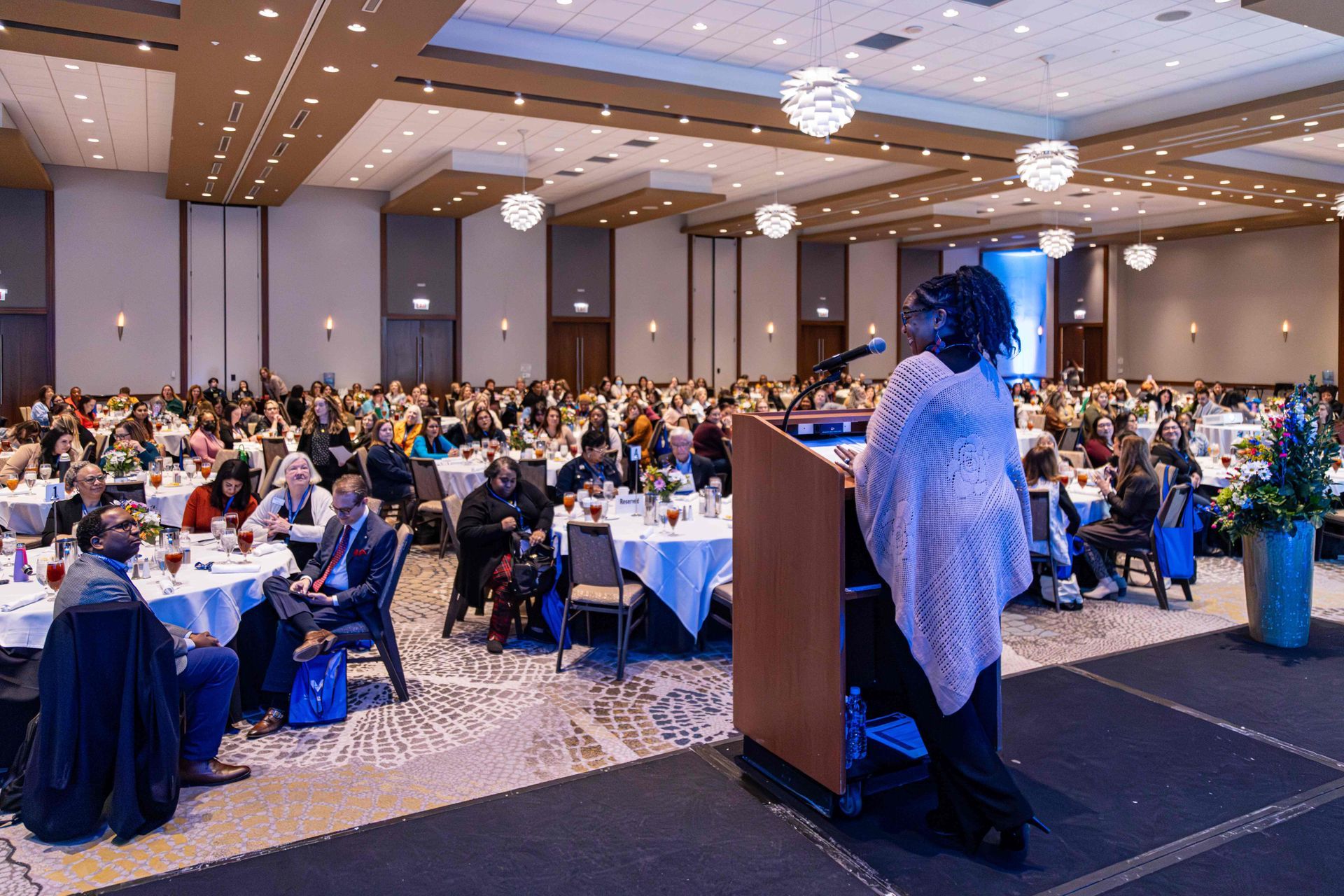 A woman is standing at a podium in front of a large crowd of people at a conference.