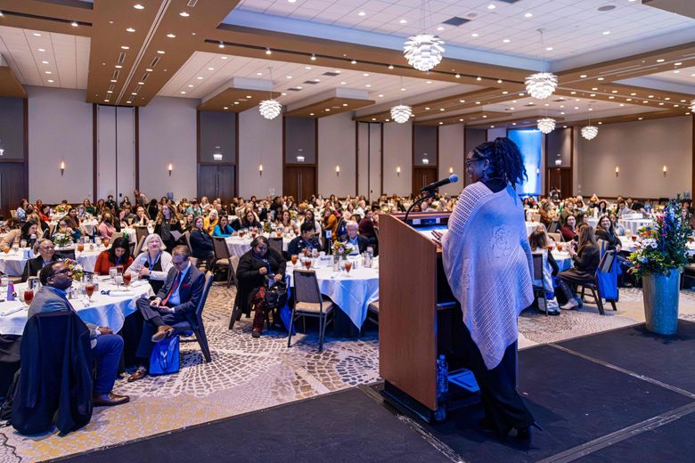 A woman is standing at a podium in front of a large crowd of people at a conference.