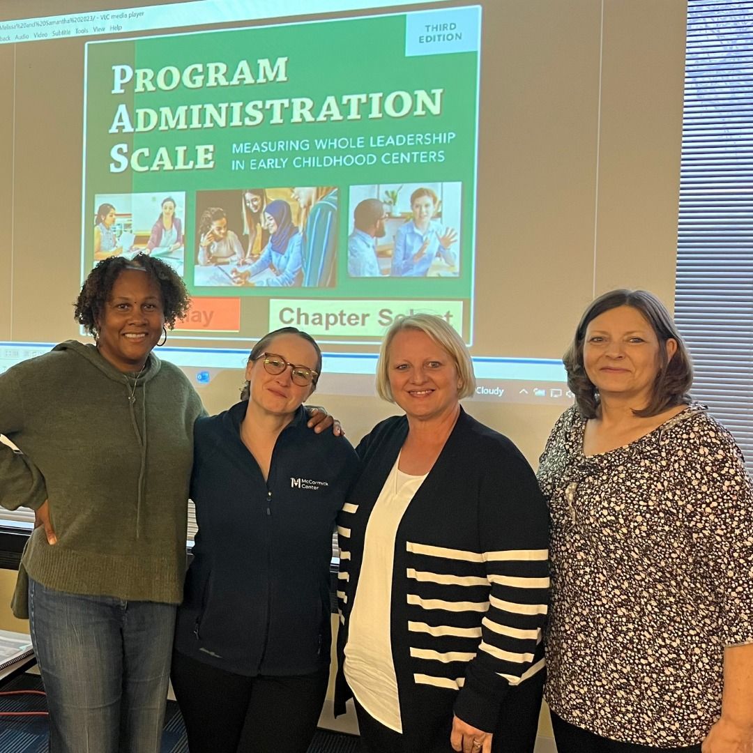 A group of women standing in front of a screen that says program administration scale A group of women standing in front of a screen that says program administration scale