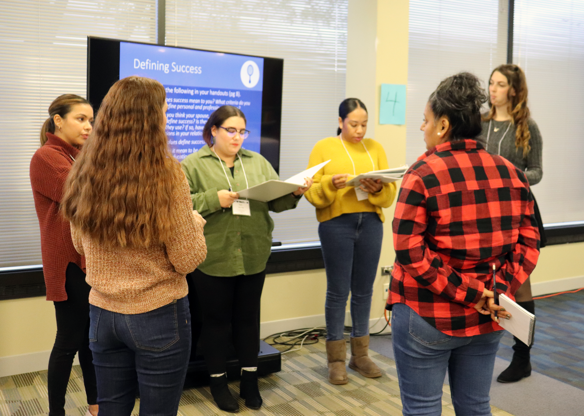Six women discussing papers in front of a screen that says