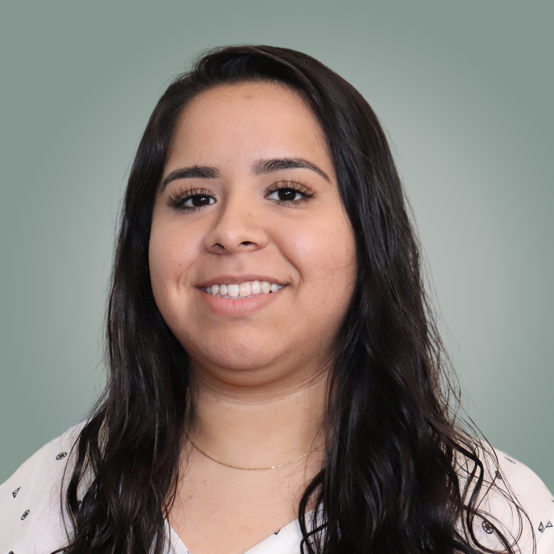 A woman with long dark hair is smiling and wearing a white shirt.