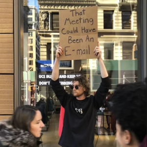 A man holds up a sign that says that meeting could have been an e-mail