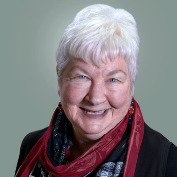 A woman with white hair and a red scarf is smiling for the camera.