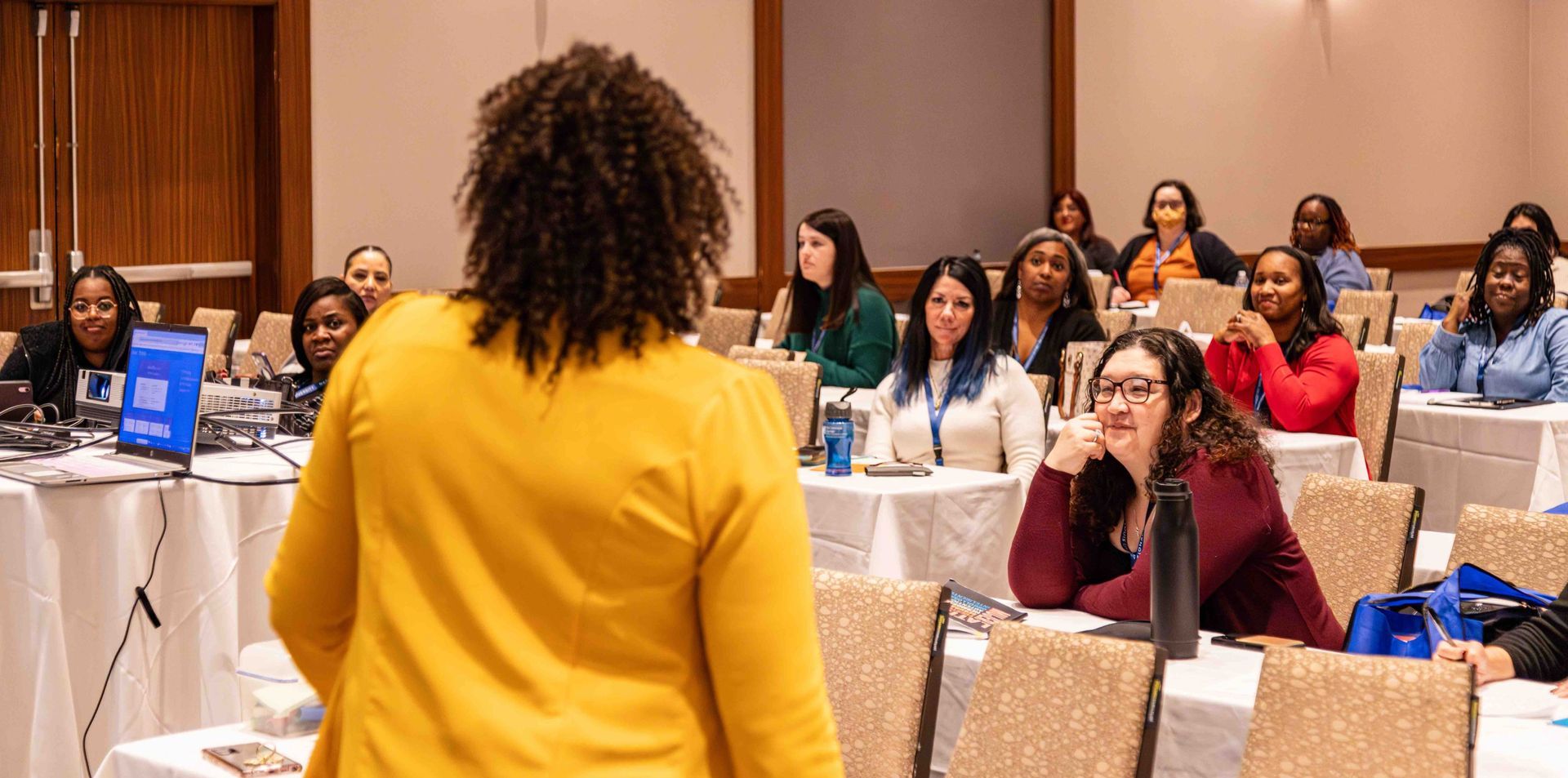 Woman at desk working on laptop, writing in notebook. Smiling, interior setting.