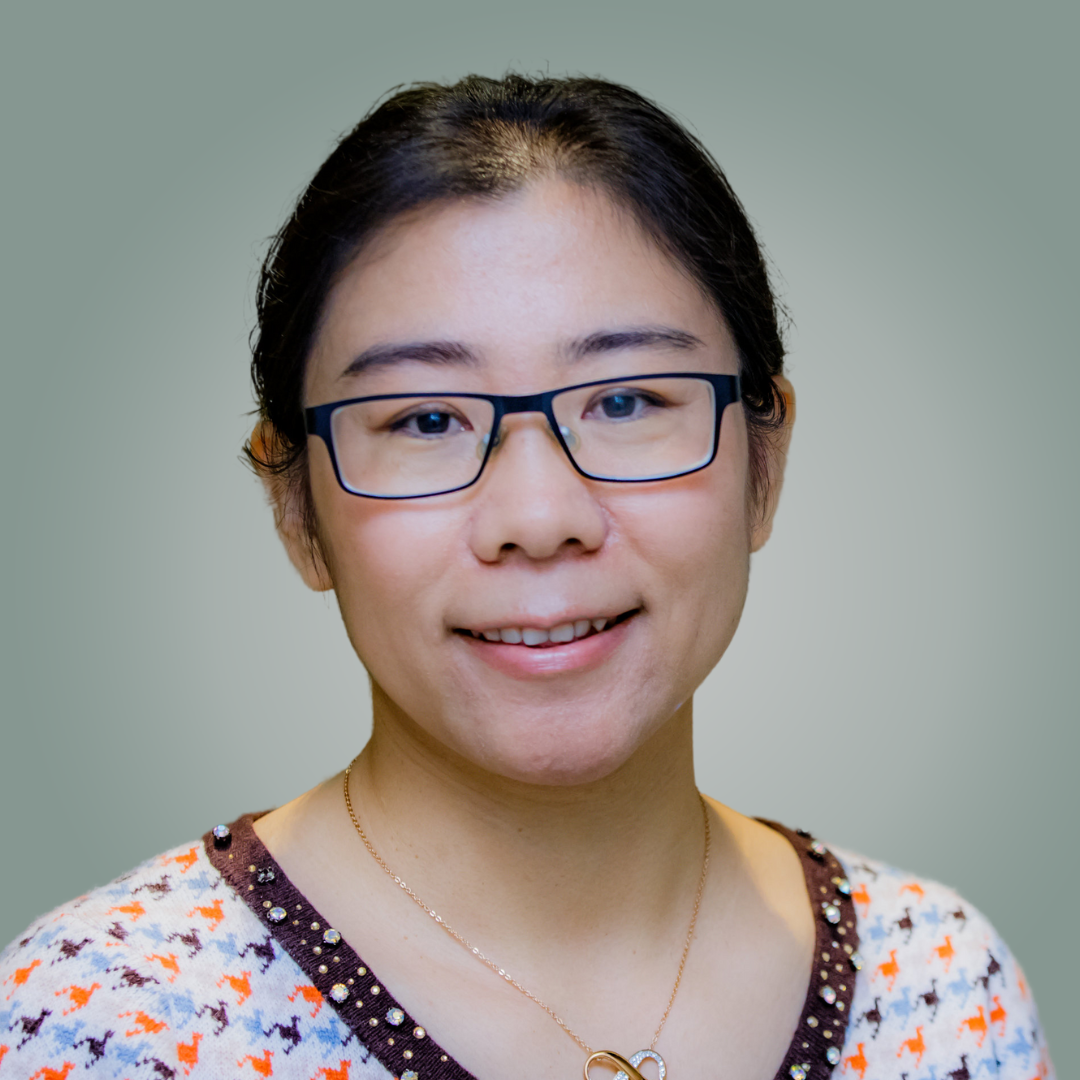 A woman wearing glasses and a necklace smiles for the camera