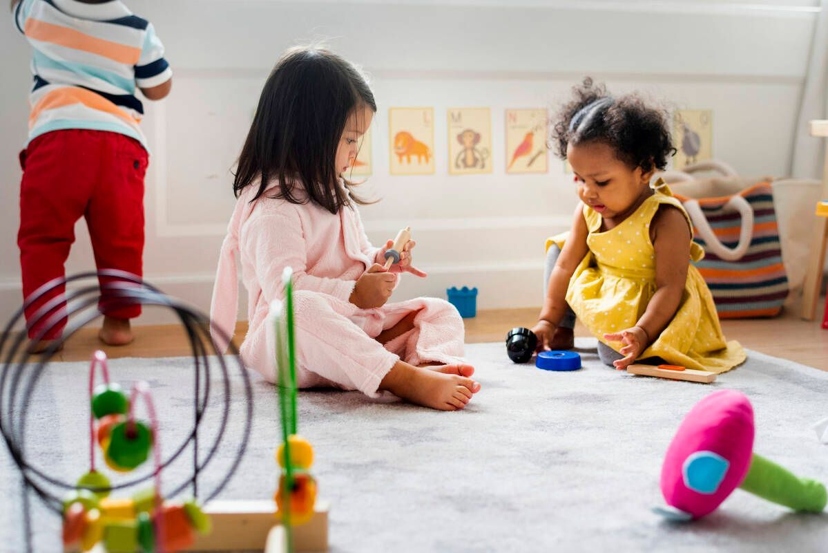 Two little girls are sitting on the floor playing with toys.