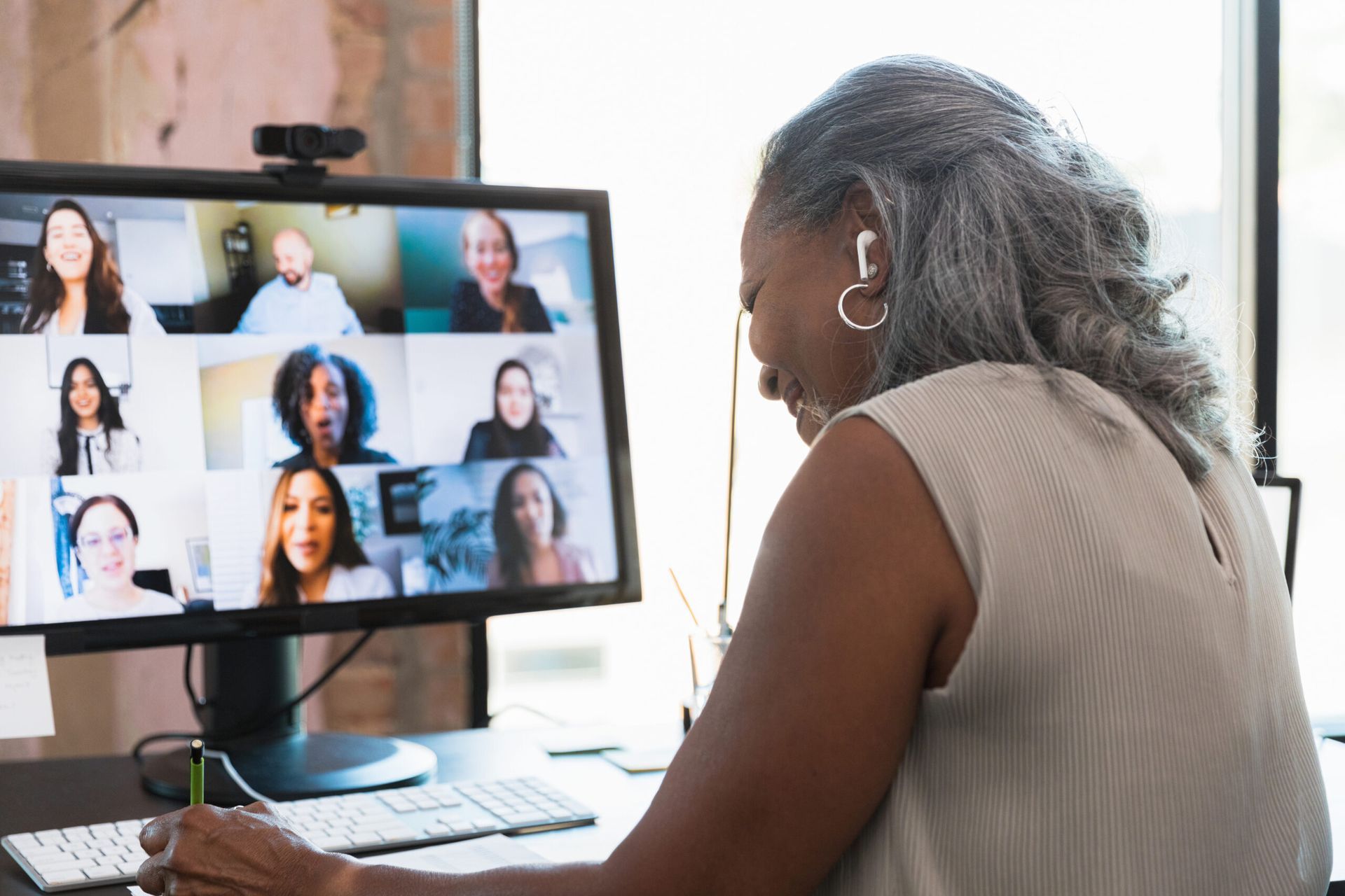 A woman is sitting in front of a computer screen having a video call with a group of people. A woman is sitting in front of a computer screen having a video call with a group of people.