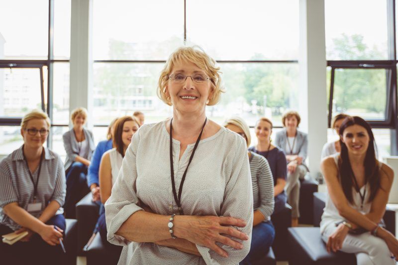 A woman is standing in front of a group of people sitting in a room.