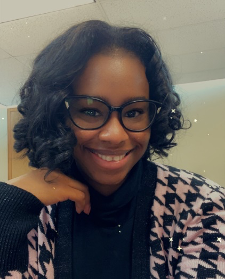 A woman wearing glasses and a plaid jacket is smiling for the camera.